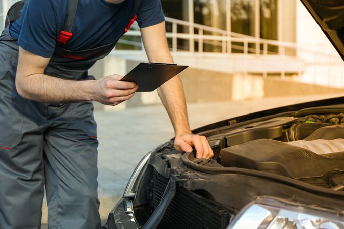 A man in overalls holds clipboard. Mechanic. Car inspection