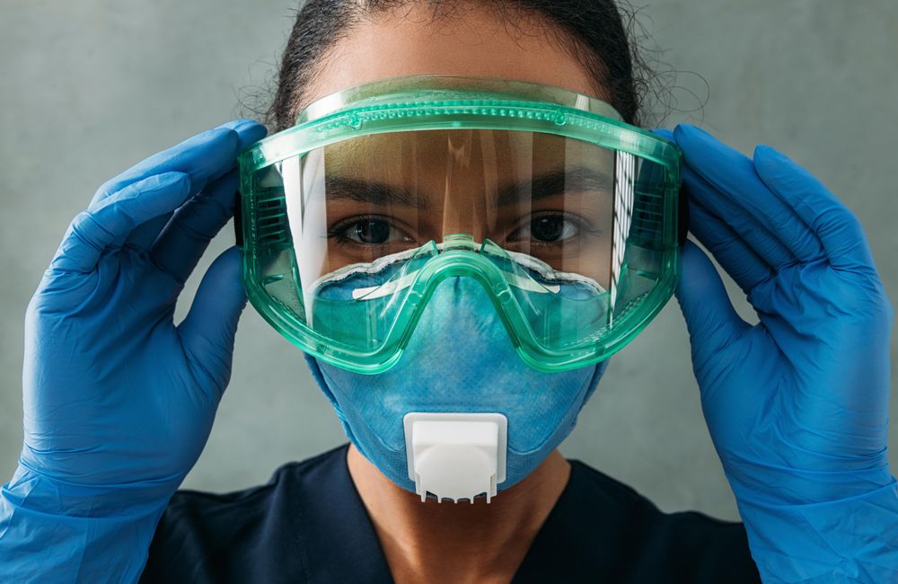 Female Black doctor’s face in PPE gear as she adjusts her eye wear