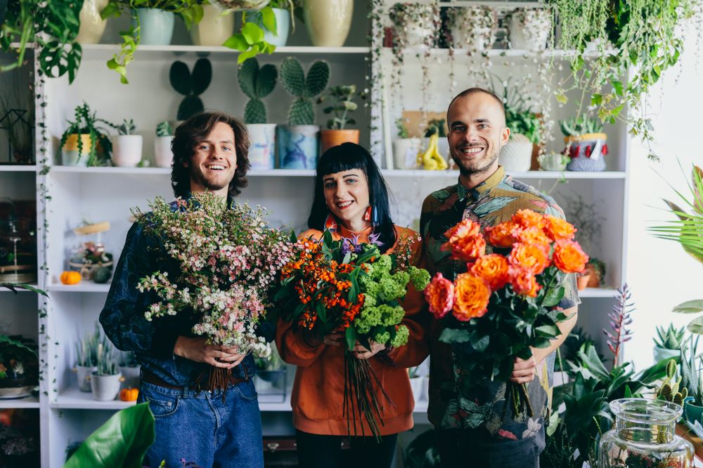 Woman and two men holding flowers in the flower shop.