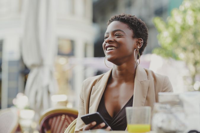 Smiling Black woman with smartphone sitting at table in cafe