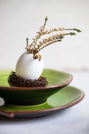Side view of Easter table setting with decorative egg, with heather on green plate