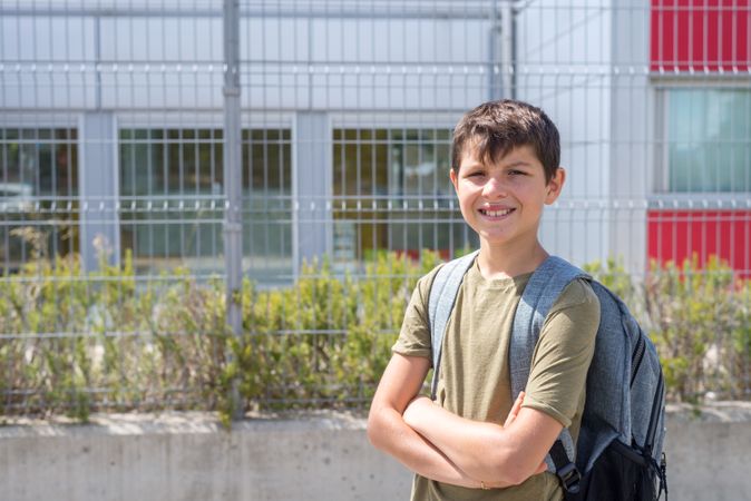 Smiling teenage boy standing outside of school with arms crossed