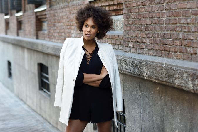 Female in dress with blazer draped over shoulders standing next to outdoor wall, copy space