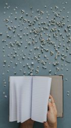 Person flipping blank notebook on blue background with tiny flowers around