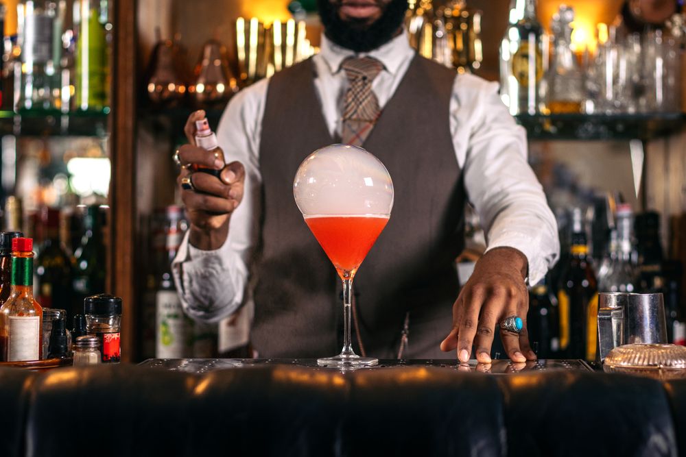 Stylish Black bartender preparing a cocktail with a smoke bubble in a traditional cocktail bar