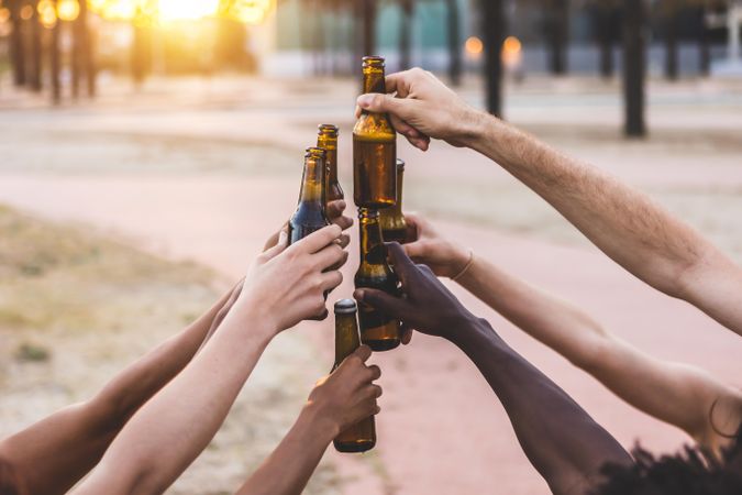 Arms of diverse friends toasting with beer at sunset