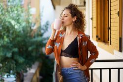 Attractive young female drinking coffee on balcony in town