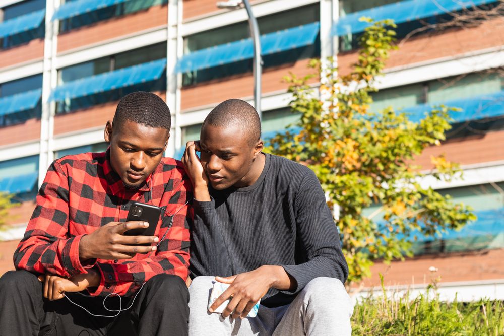 Positive Black men using smartphones together in park