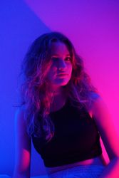 Teenage girl in dark top sitting in purple lit studio