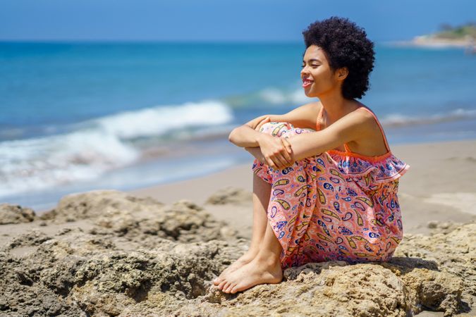 Happy woman sitting on the rocks on the coast looking out to the sea