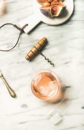 Rose wine in glass on marble table with quartered fig, knife and corkscrew