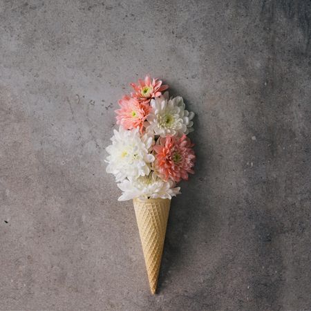 Pink and light colored flowers in ice cream cone on marble background