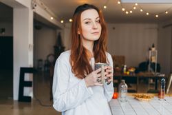 Woman looks up while holding mug of a warm drink in her apartment