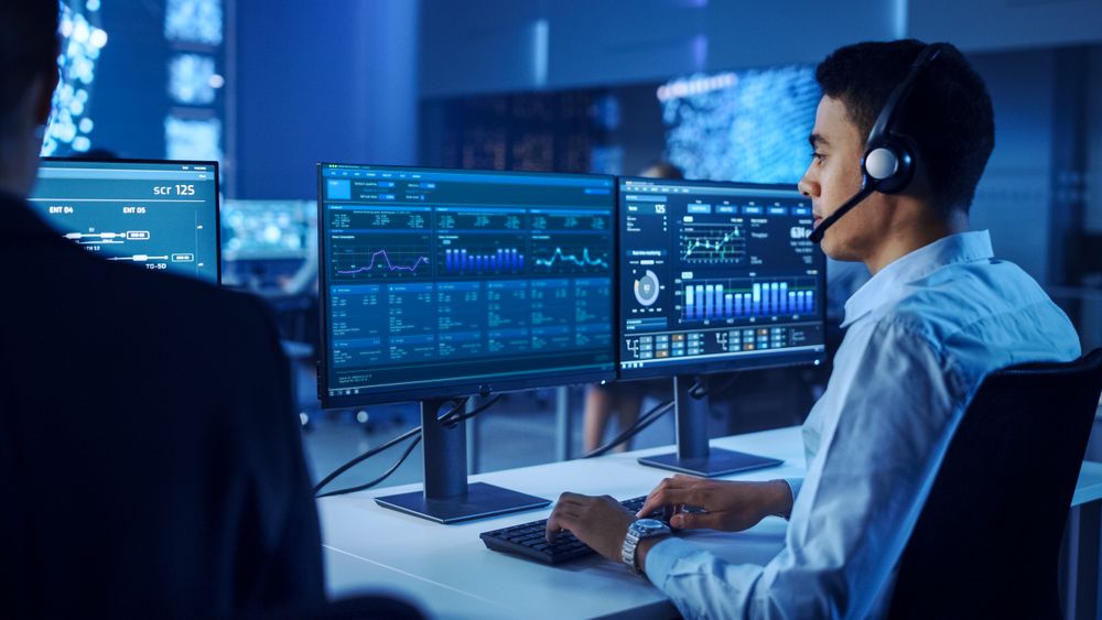Focused Professional Analyzes Complex Data on Dual Monitors in a High-tech Control Room, Enhancing Cybersecurity and Operational Efficiency. the Environment Fosters Innovation and Strategic Decision-making.
