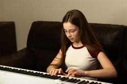 Young pianist in glasses playing keyboard with serious focus