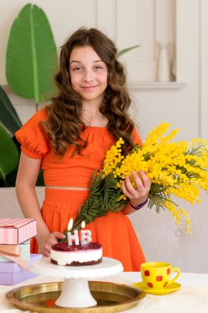 Girl in orange dress holding yellow flowers with birthday cake