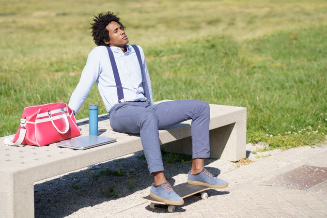 Man with eyes closed on concrete bench with skateboard