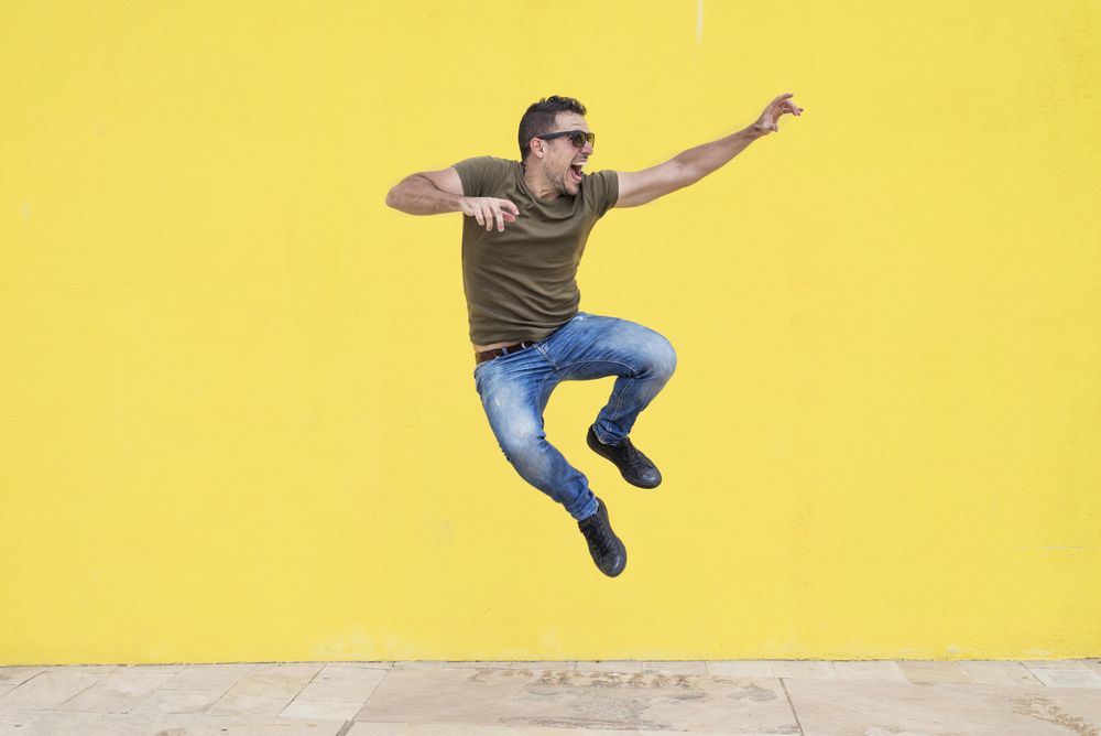 Happy male jumping in front of yellow wall and looking to the side