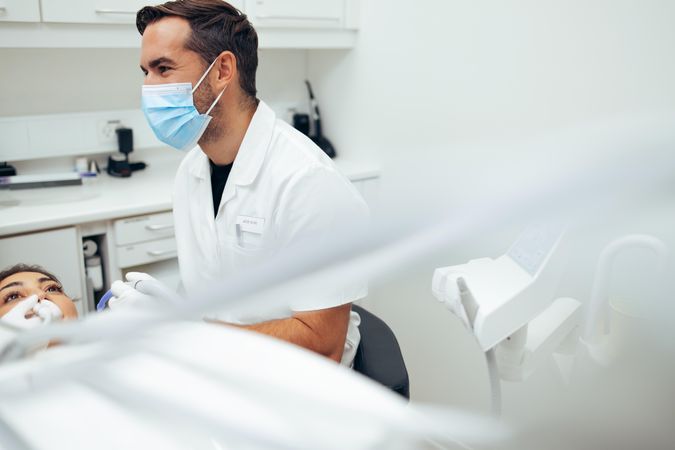 Male dentist talking with his assistant while examining female patient's teeth