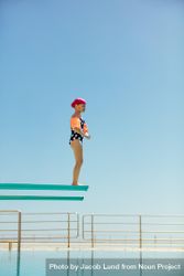 Girl preparing to jump off a diving board against clear blue sky 499vy4