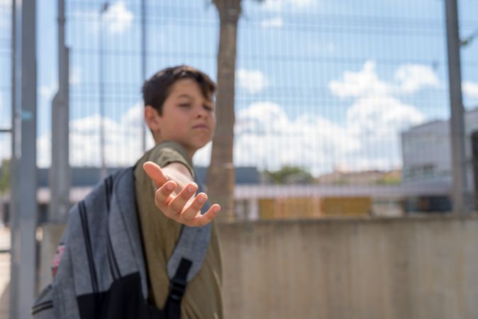 Teenager standing outside school gate with hand reaching back