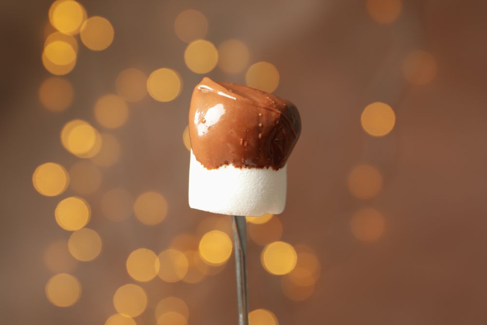 Marshmallow in chocolate against brown background with blurred lights