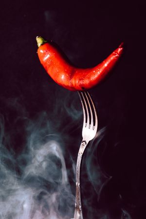 red chili pepper in fork on a dark background with smoke