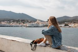 Woman sitting on ledge near the water talking on a smartphone