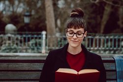 Young woman reading book on bench in park
