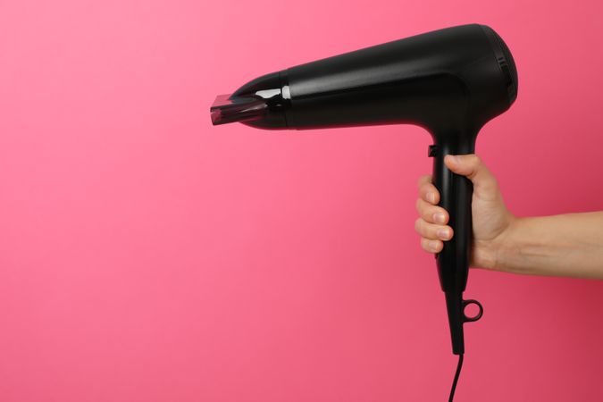 Female hand holds hair dryer on pink background, space for text