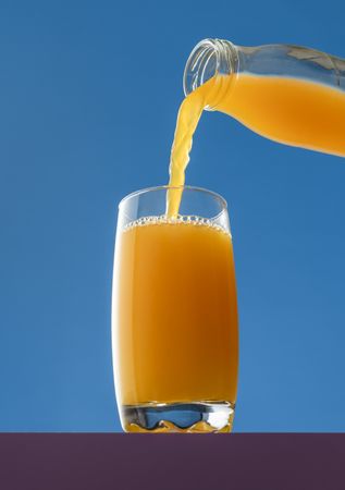Pouring orange juice into a glass, isolated on a blue background