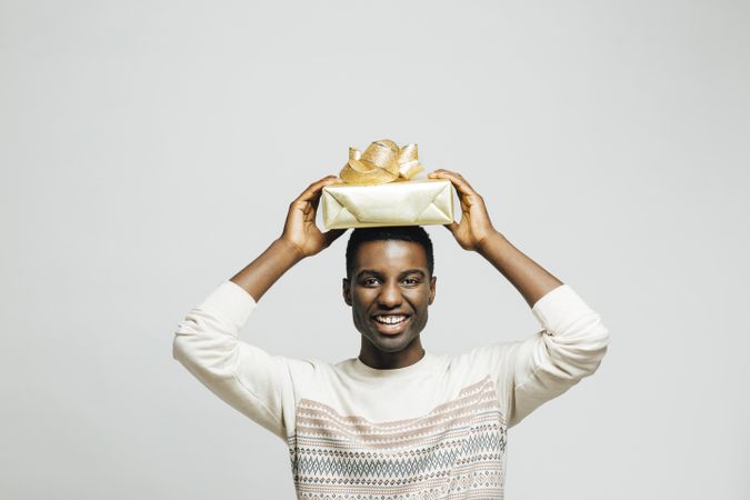 Smiling Black man holding present wrapped in gold paper above his head