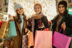 Three happy friends holding shopping bags at a Christmas market and looking at the camera.