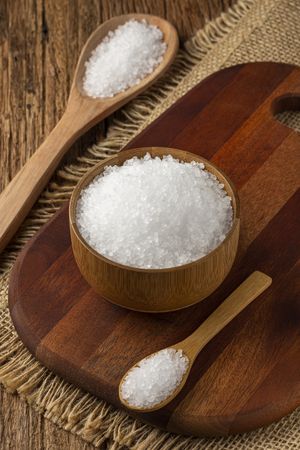 Coarse salt in bowl on wooden background.