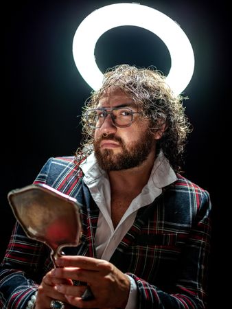 Serious man with glowing fake nimbus holding mirror and looking at camera