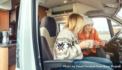Side view of female friends sitting in parked van having coffee and checking social media on phone 56qQN0