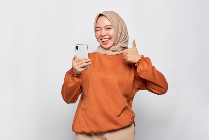 Happy Muslim woman in headscarf and orange shirt pointing at phone