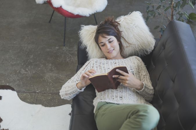 Above view of female lying back reading book on leather sofa