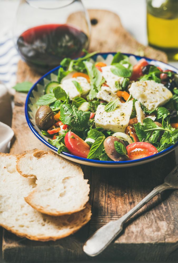 Greek salad with feta, tomatoes, and red wine on wooden board, vertical composition, close up