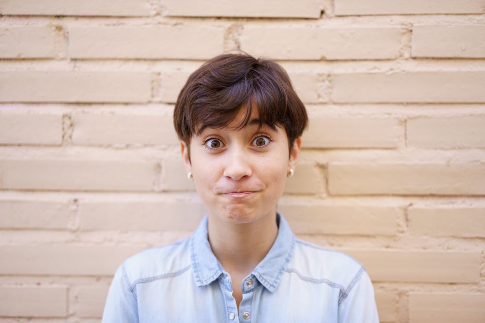 A surprised young woman sporting a trendy short hairstyle stands against a neutral backdrop