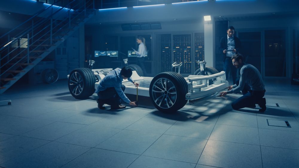 Automobile Engineer Working on Electric Car Chassis Platform, Using Tablet Computer Augmented Reality with 3D CAD Software Modelling.