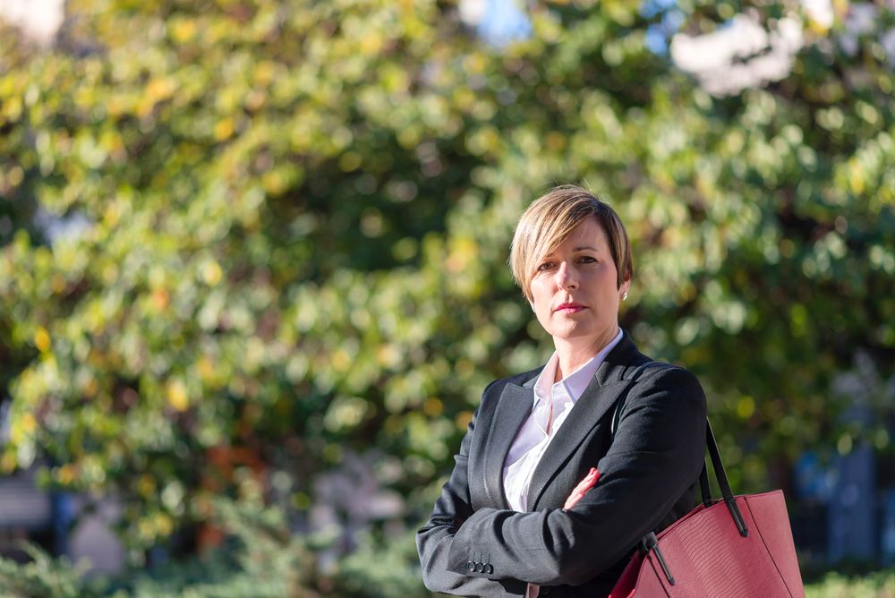 Businesswoman standing with arms crossed in front of hedge