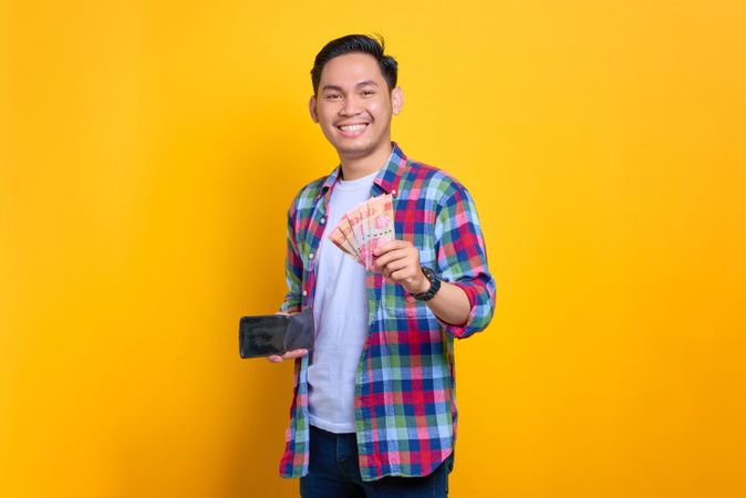 Asian man smiling while holding cash out of his wallet