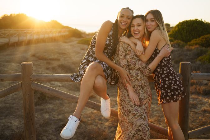 Close women in summer dresses sitting on wooden fence at magic hour