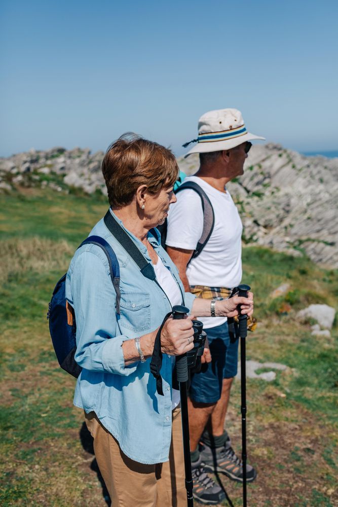 Mature man and woman with poles hiking outdoors, vertical