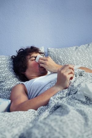Sick man blowing nose and checking temperature in bed