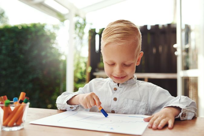 Smiling blond boy drawing outside on deck