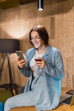 Young businesswoman with wine using smartphone