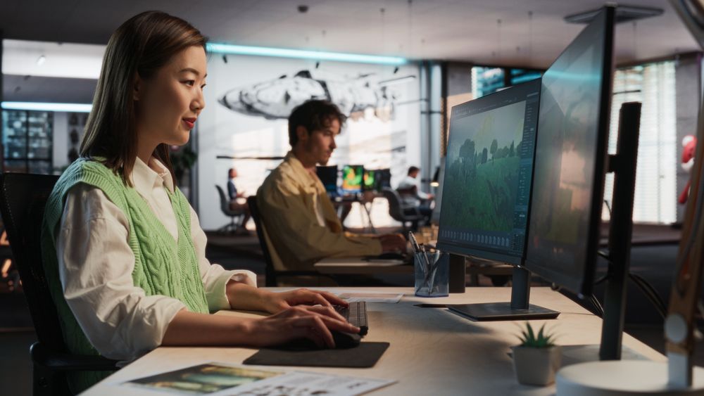 Asian Woman Using Desktop Computer And Designing In 3D Modelling Software Unique World And Characters For Survival Video Game In Diverse Office.