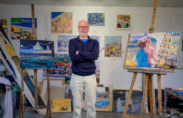 Proud male artist with arms crossed surrounded by paintings in art studio
